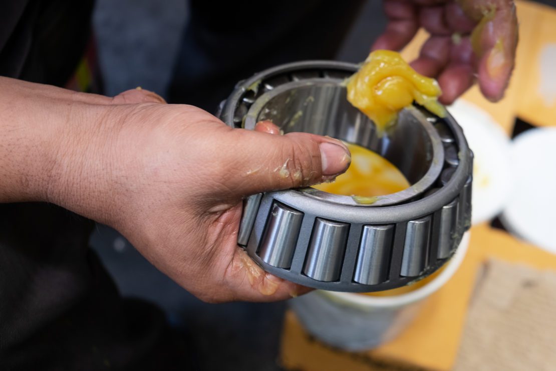 close up of technician's hands as he puts NLGI 3 yellow lithium grease onto a wheel bearing for a ten-wheel truck